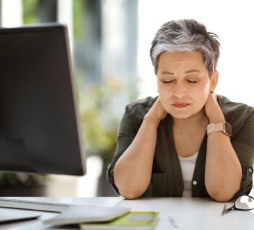 Woman sitting at desk with eyes closed, rubbing neck