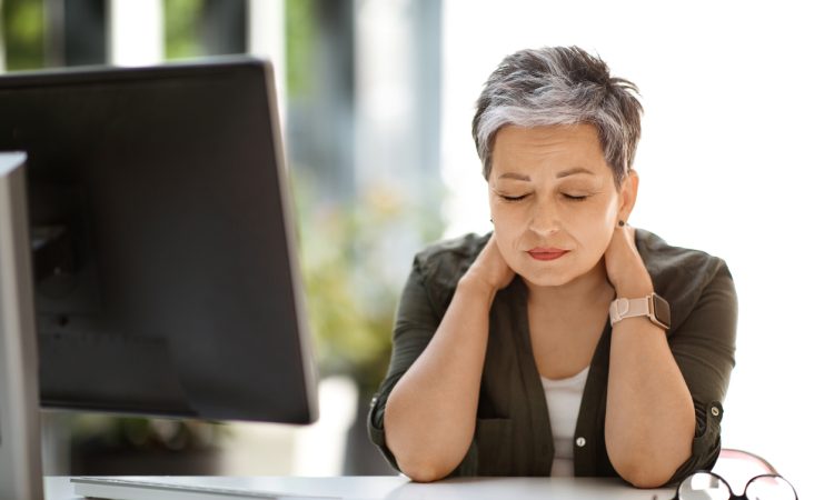 Woman sitting at desk with eyes closed, rubbing neck