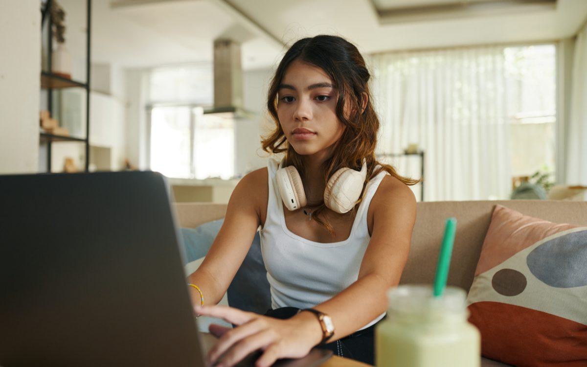 Serious teenage girl with headphones working on laptop
