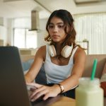 Serious teenage girl with headphones working on laptop