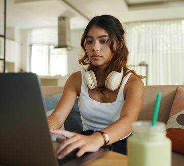Serious teenage girl with headphones working on laptop