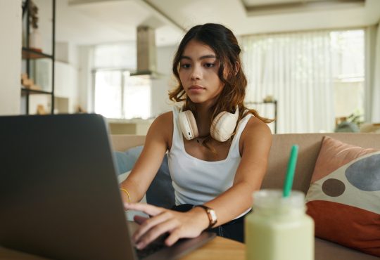 Serious teenage girl with headphones working on laptop