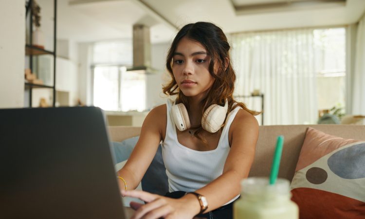 Serious teenage girl with headphones working on laptop