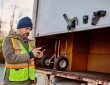 Delivery truck driver standing behind box, checking phone