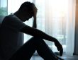 Man silhouetted sitting beside window with head in hands