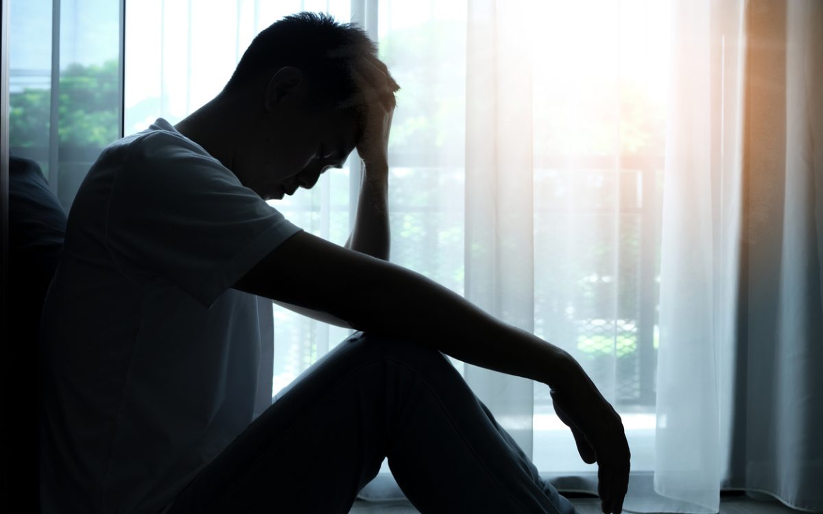 Man silhouetted sitting beside window with head in hands