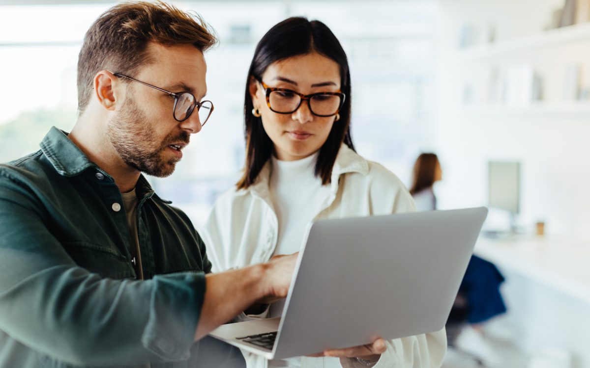 Two people standing and talking while looking at laptop in office