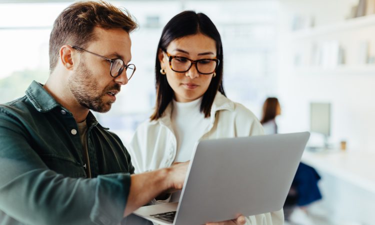 Two people standing and talking while looking at laptop in office