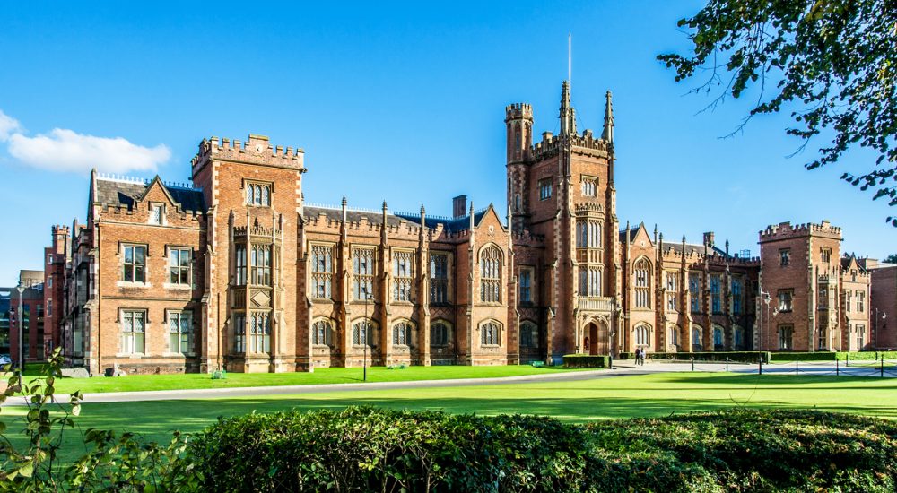 The Queen's University of Belfast with a grass lawn, tree branches and a hedge in sunset light