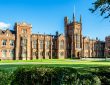 The Queen's University of Belfast with a grass lawn, tree branches and a hedge in sunset light