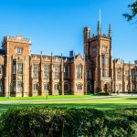 The Queen's University of Belfast with a grass lawn, tree branches and a hedge in sunset light