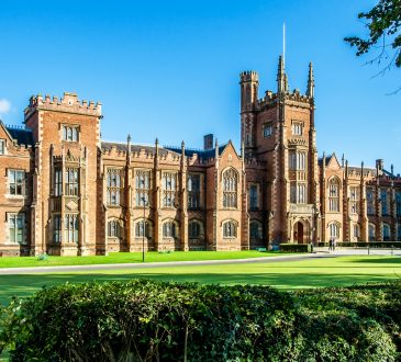 The Queen's University of Belfast with a grass lawn, tree branches and a hedge in sunset light