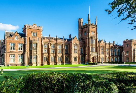 The Queen's University of Belfast with a grass lawn, tree branches and a hedge in sunset light