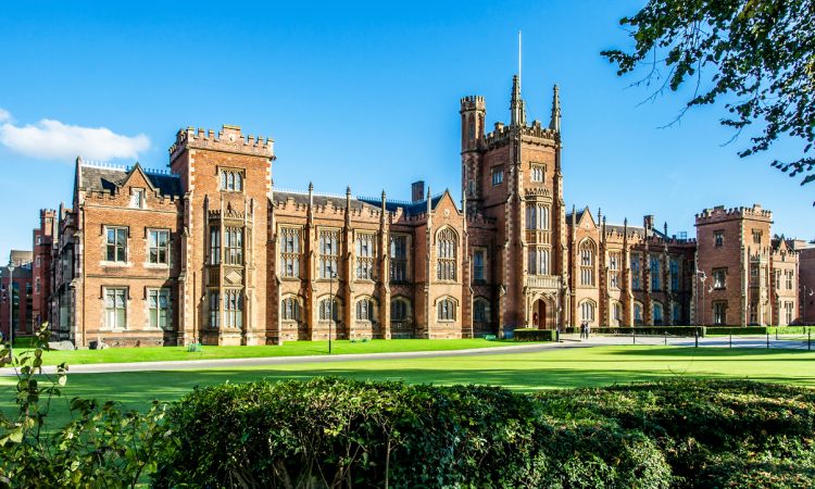The Queen's University of Belfast with a grass lawn, tree branches and a hedge in sunset light