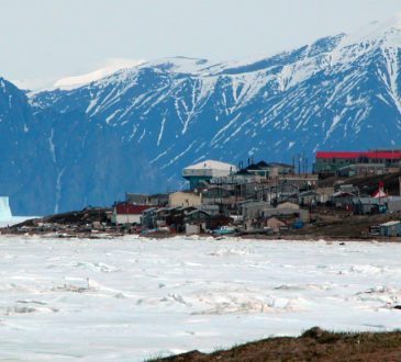 n Photo of Pond Inlet in mid June of 2005 from Salmon Creek, 3.5 kms West of the Hamlet. The mountains are 25kms away and the iceberg is 9kms from town. The community's library (large white roof) and Health Center (large red roof) are the most predominent structures in the photo.