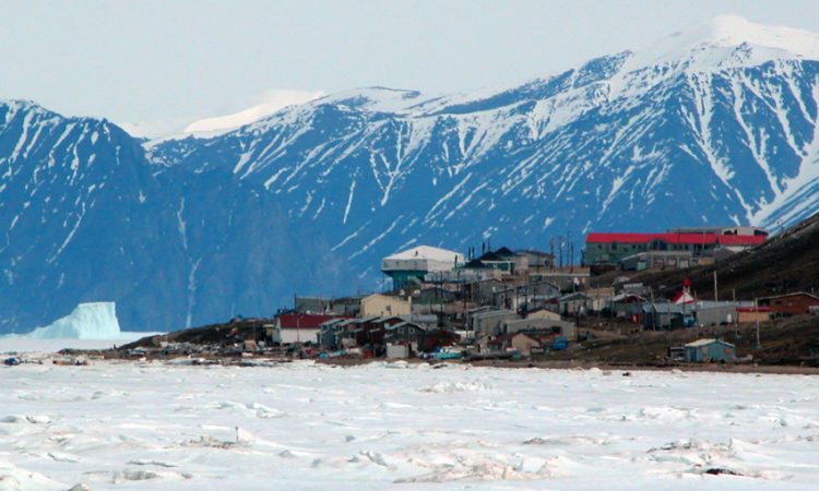 n Photo of Pond Inlet in mid June of 2005 from Salmon Creek, 3.5 kms West of the Hamlet. The mountains are 25kms away and the iceberg is 9kms from town. The community's library (large white roof) and Health Center (large red roof) are the most predominent structures in the photo.