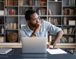Man sitting at laptop thinking with hand on chin
