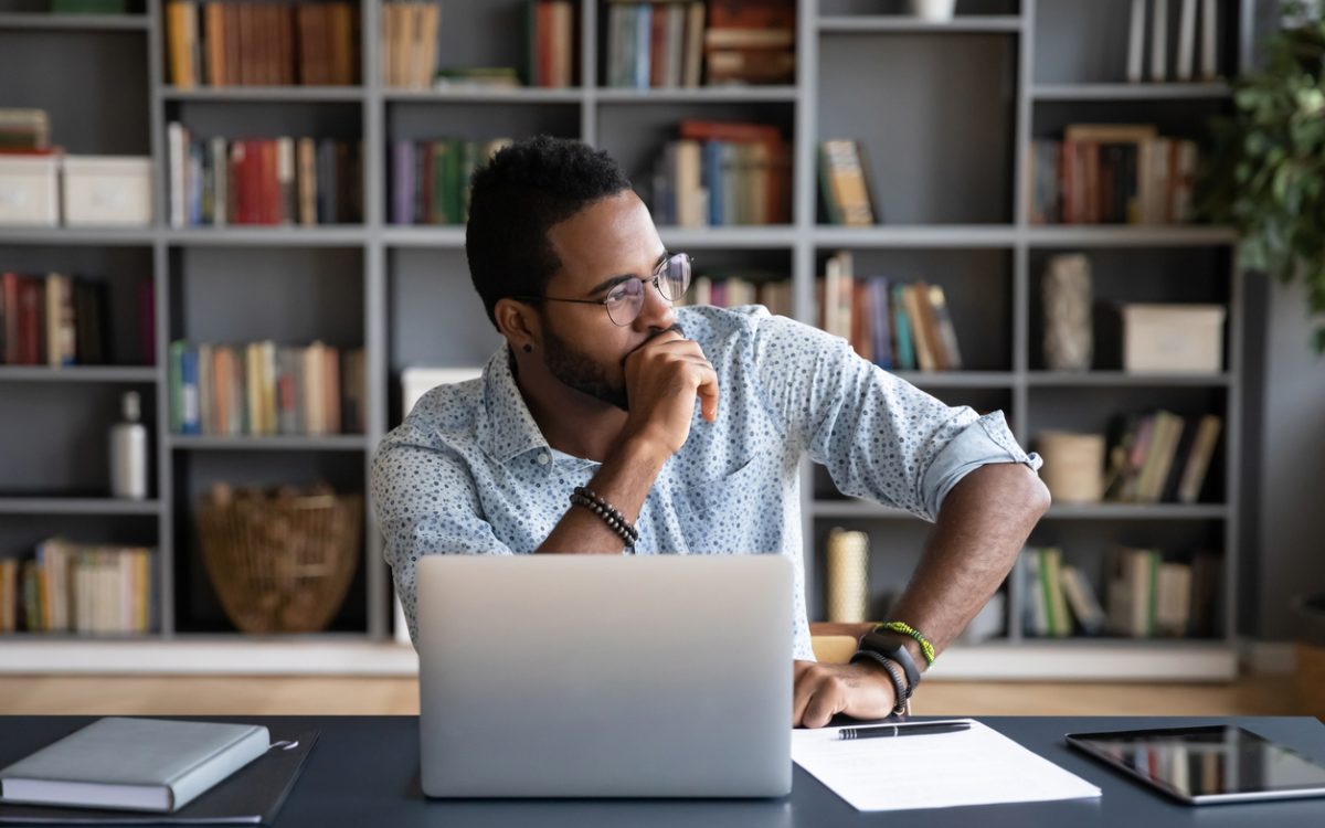 Man sitting at laptop thinking with hand on chin