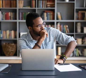 Man sitting at laptop thinking with hand on chin