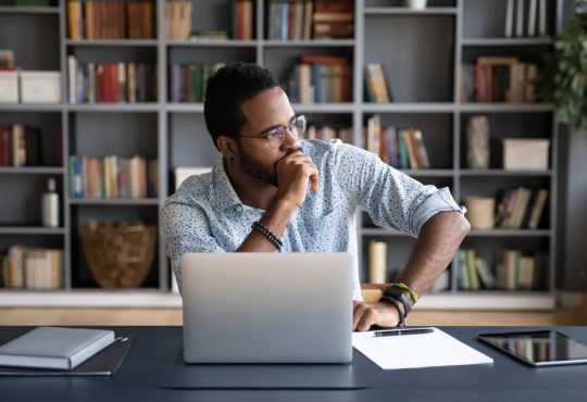 Man sitting at laptop thinking with hand on chin