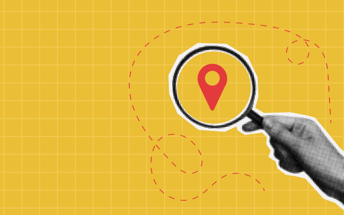 Photo illustration of hand holding magnifying glass on top of map