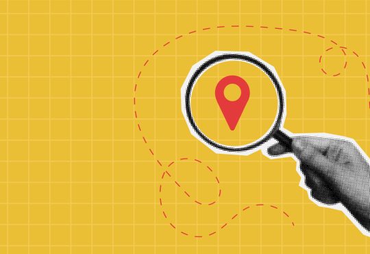 Photo illustration of hand holding magnifying glass on top of map