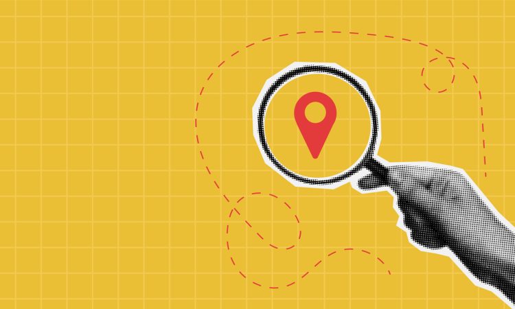 Photo illustration of hand holding magnifying glass on top of map