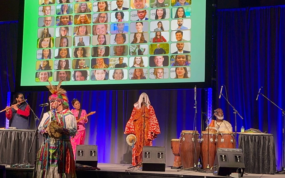 An image of the cultural celebration at Cannexus26 with indigenous music performers holding instruments on a stage. Behind them is a blue curtain and a slide showing photos of CERIC board and staff headshots.