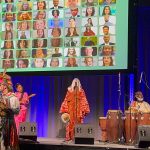 An image of the cultural celebration at Cannexus26 with indigenous music performers holding instruments on a stage. Behind them is a blue curtain and a slide showing photos of CERIC board and staff headshots.