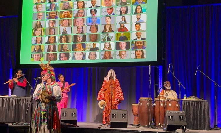 An image of the cultural celebration at Cannexus26 with indigenous music performers holding instruments on a stage. Behind them is a blue curtain and a slide showing photos of CERIC board and staff headshots.