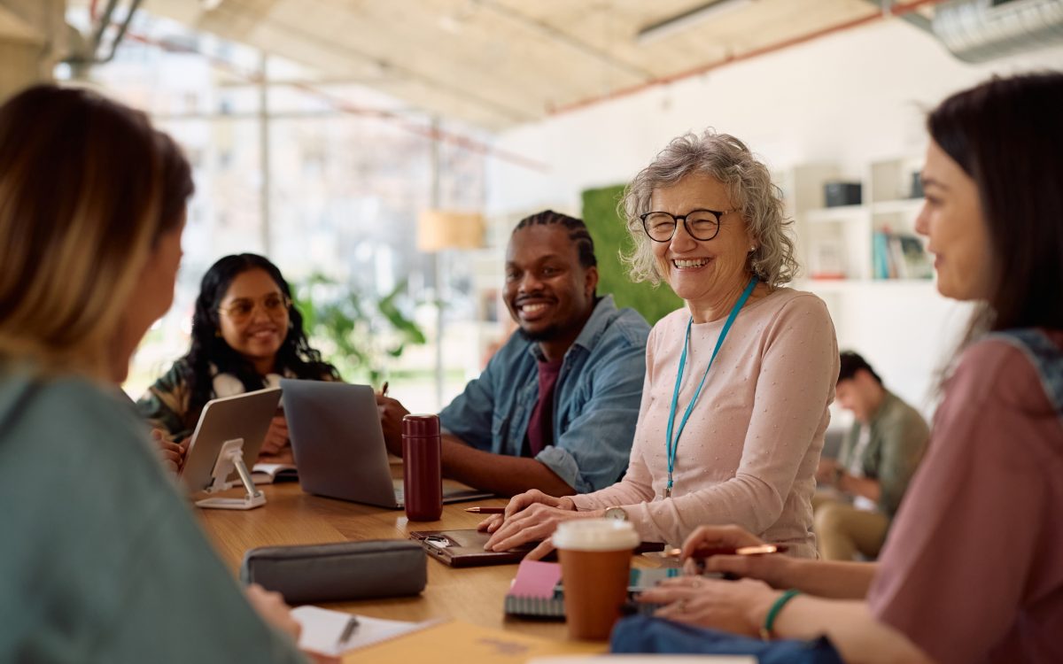 Happy mature professor and her students talking at university classroom.