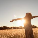 Happy little boy child standing in a meadow with arms outstretched.