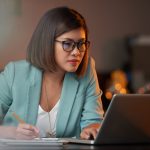 Young Vietnamese business woman working on laptop and taking notes
