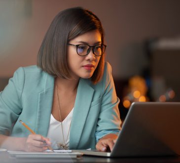 Young Vietnamese business woman working on laptop and taking notes
