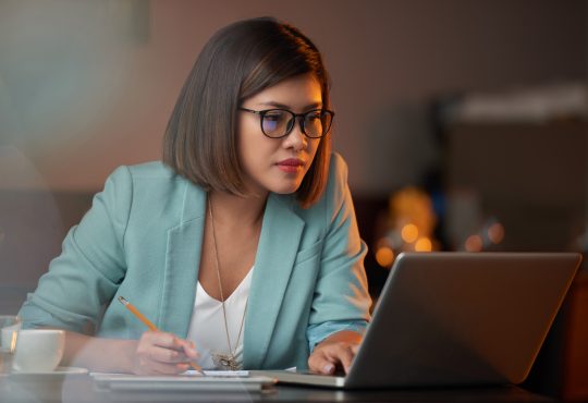 Young Vietnamese business woman working on laptop and taking notes