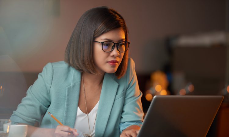 Young Vietnamese business woman working on laptop and taking notes