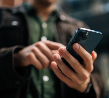 Close-up hands of unrecognizable man holding and using smartphone standing on city street, browsing internet, checking social media, using mobile application. Concept of modern communication.