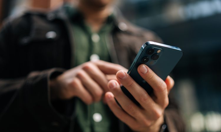 Close-up hands of unrecognizable man holding and using smartphone standing on city street, browsing internet, checking social media, using mobile application. Concept of modern communication.