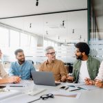 A diverse office team is engaged in a strategic meeting, with a senior colleague leading discussion, illustrating a productive and inclusive workplace. Colleagues engage in a lively exchange of ideas
