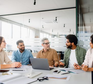 A diverse office team is engaged in a strategic meeting, with a senior colleague leading discussion, illustrating a productive and inclusive workplace. Colleagues engage in a lively exchange of ideas