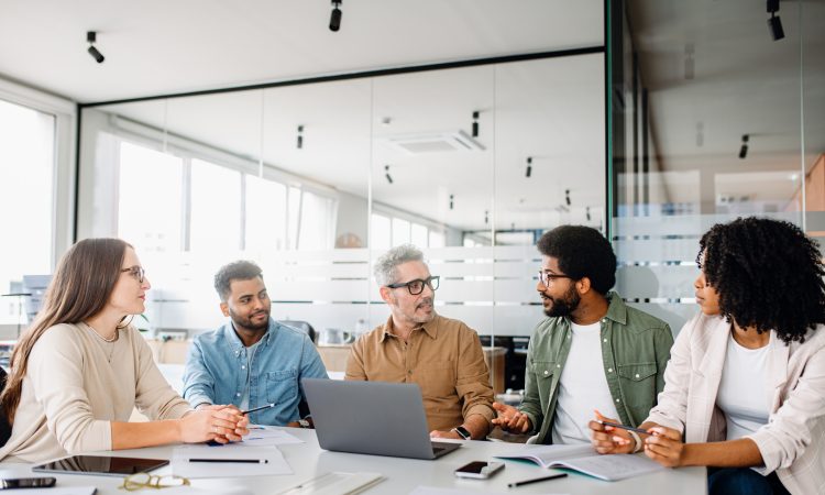 A diverse office team is engaged in a strategic meeting, with a senior colleague leading discussion, illustrating a productive and inclusive workplace. Colleagues engage in a lively exchange of ideas