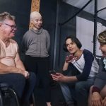 Smiling friends, including man in wheelchair, sitting and talking in gym after workout