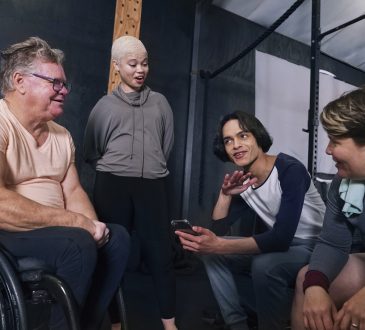 Smiling friends, including man in wheelchair, sitting and talking in gym after workout