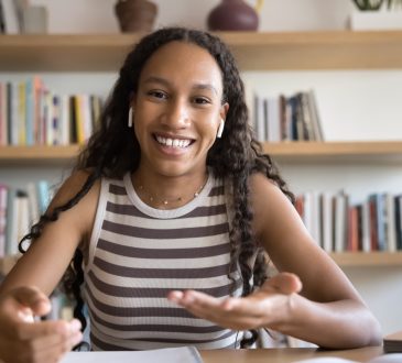 Webcam view of African student girl wear earphones looking at camera and speaking, participate in education webinar, talking with tutor, discussing joint schoolwork with groupmate using video call app