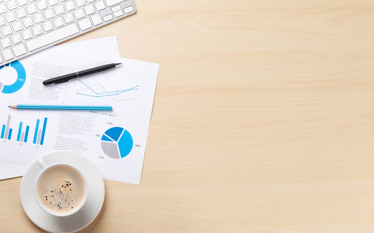 Office desk workplace with pc, charts and coffee on wooden table. Top view with copy space