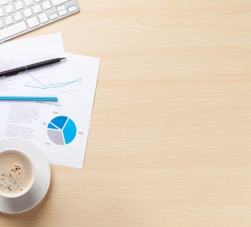 Office desk workplace with pc, charts and coffee on wooden table. Top view with copy space