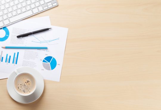 Office desk workplace with pc, charts and coffee on wooden table. Top view with copy space