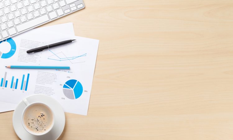 Office desk workplace with pc, charts and coffee on wooden table. Top view with copy space