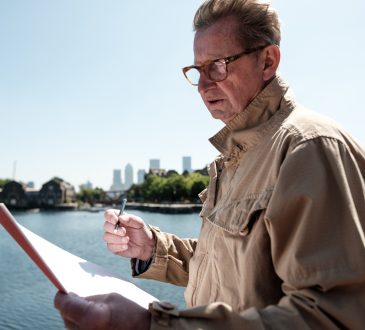 Senior engineer examining architectural plans near the river, with the iconic canary wharf skyline in the background, enjoying a sunny day in vibrant london