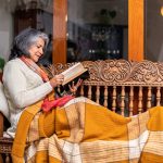 Cozy scene of a senior woman relaxing on a wooden bench with a blanket, reading a book and enjoying the comfort of her home
